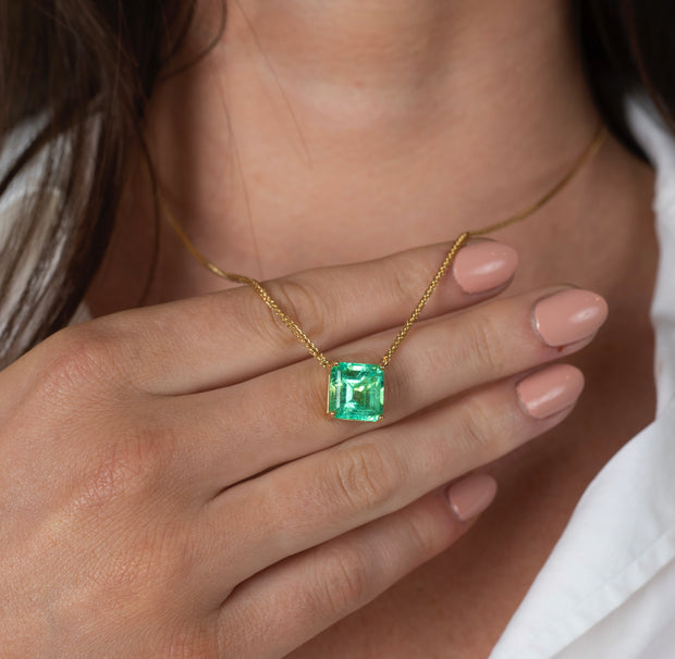 Gold necklace with a green gemstone held by a hand
